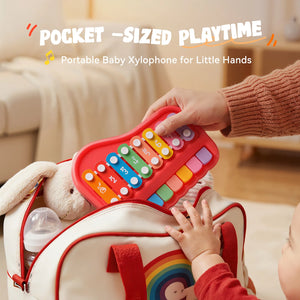 Portable baby xylophone for little hands held by a child with a hand reaching out to touch it.